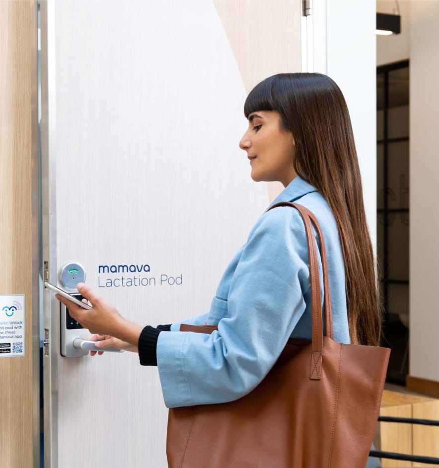 A woman in a blue shirt with a brown tote bag over her shoulder using a digital keypad to access a Mamava Lactation Pod.